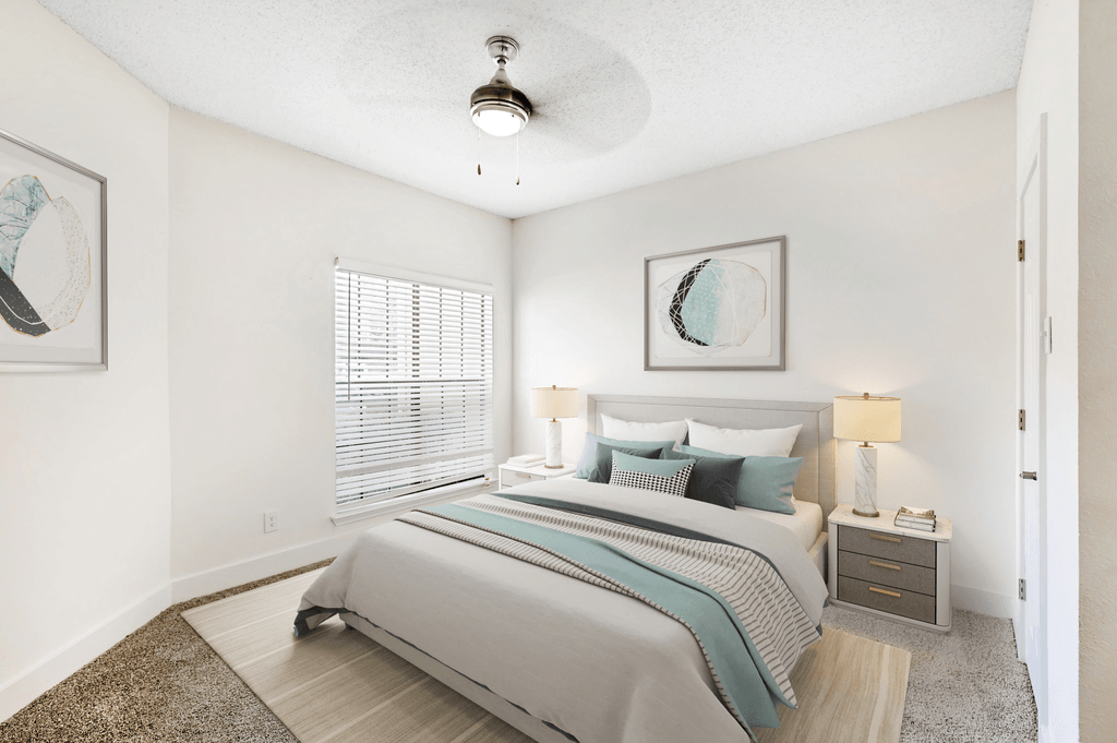 Virtually staged bedroom with carpet, accent rug, bed, nightstands with lamps, ceiling fan with light and large window with blinds